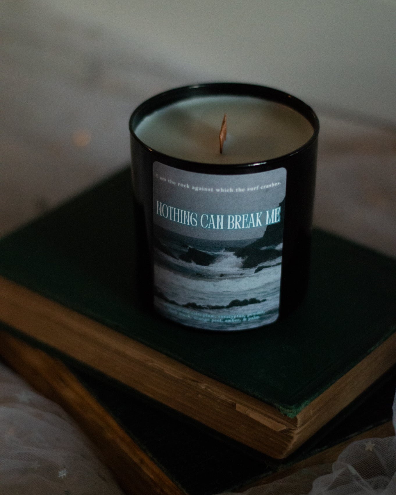 Candle in black jar with label on it that has ocean waves and the SJM quote I am the rock against which the surf crashes. Nothing can break me